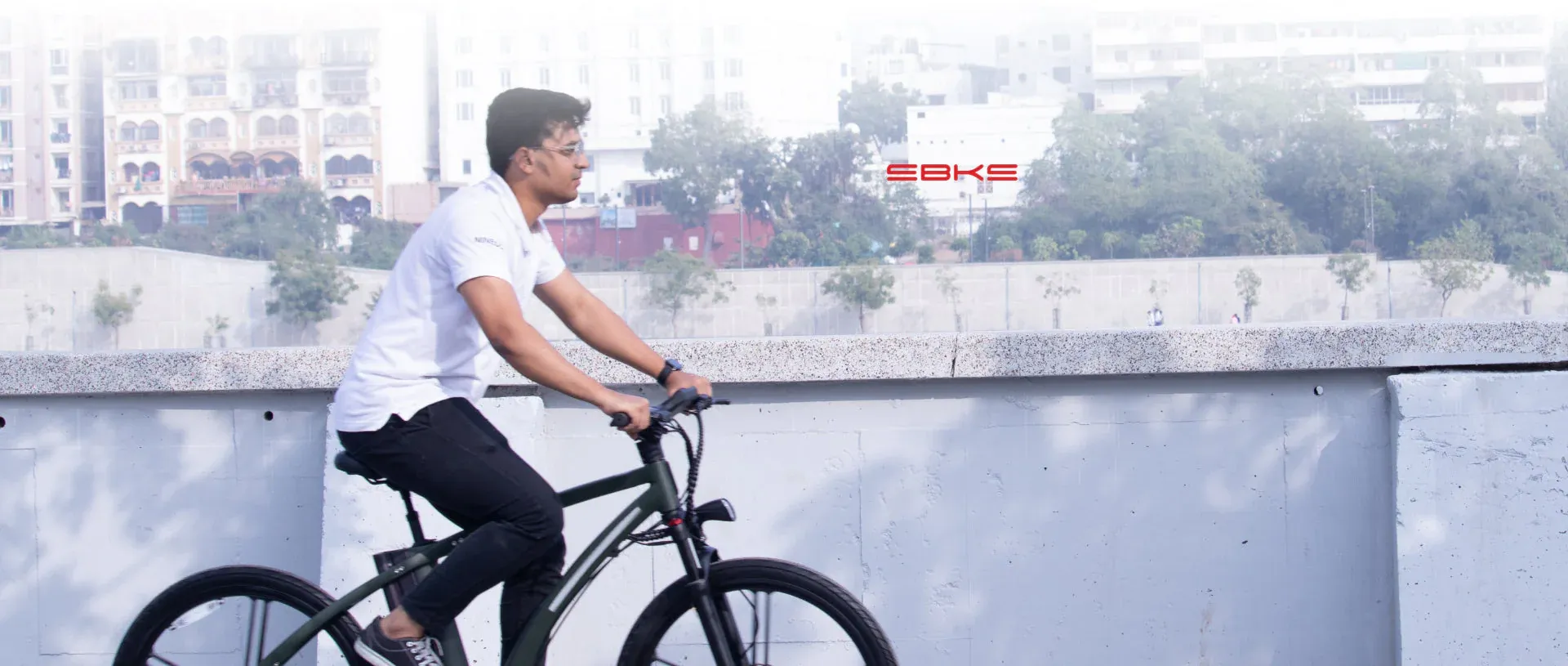Commuter riding a green NINE09 electric bike along a riverside wall in the city